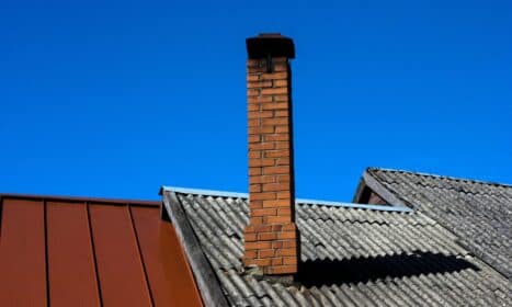 A solitary brick chimney rises from a tiled roof under a vibrant blue sky, showcasing minimal architecture.