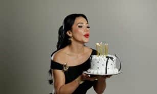 Elegant woman blowing out candles on a stylish birthday cake.