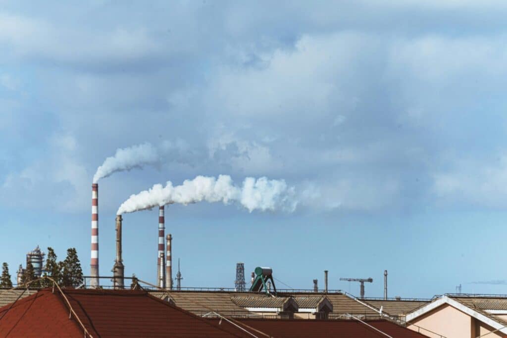 Factory chimneys emitting smoke over rooftops on a clear day, illustrating urban pollution.