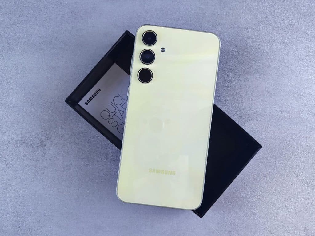 Yellow Samsung smartphone displayed on a gray surface with its box and quick start guide.