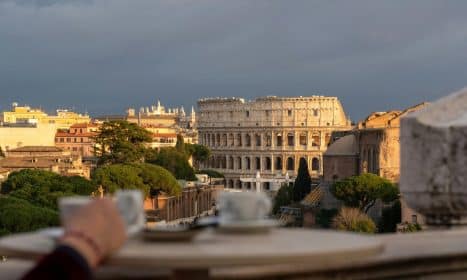 Scenic view of Rome's Colosseum at sunset, framed by a cafe table with coffee cups.
