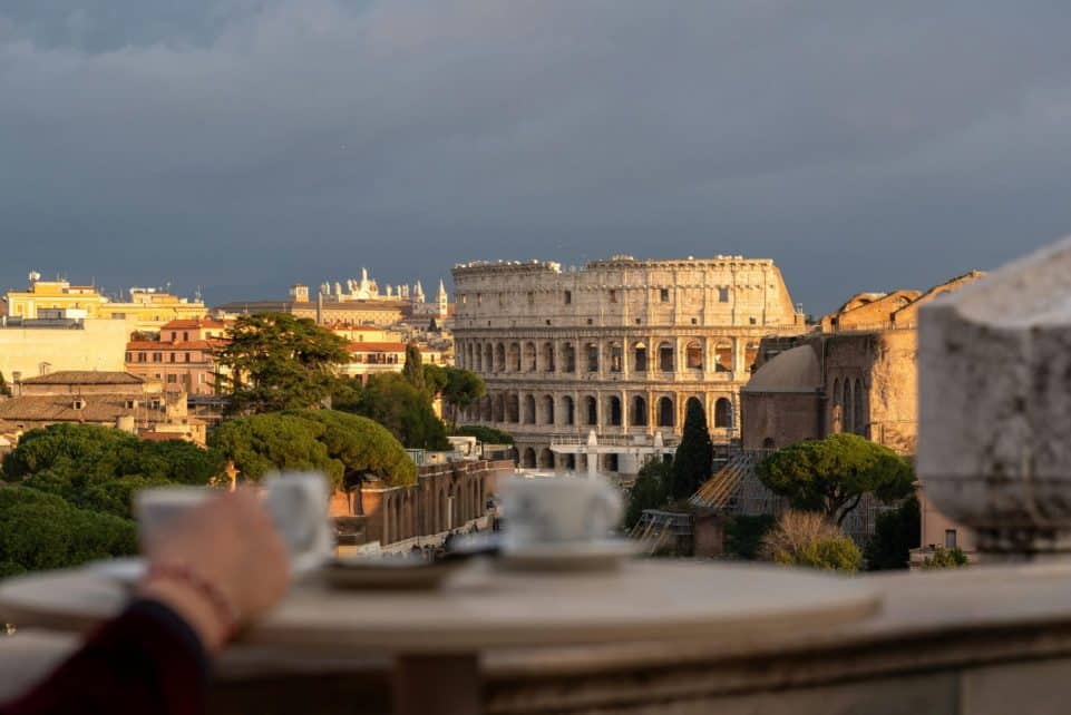Scenic view of Rome's Colosseum at sunset, framed by a cafe table with coffee cups.