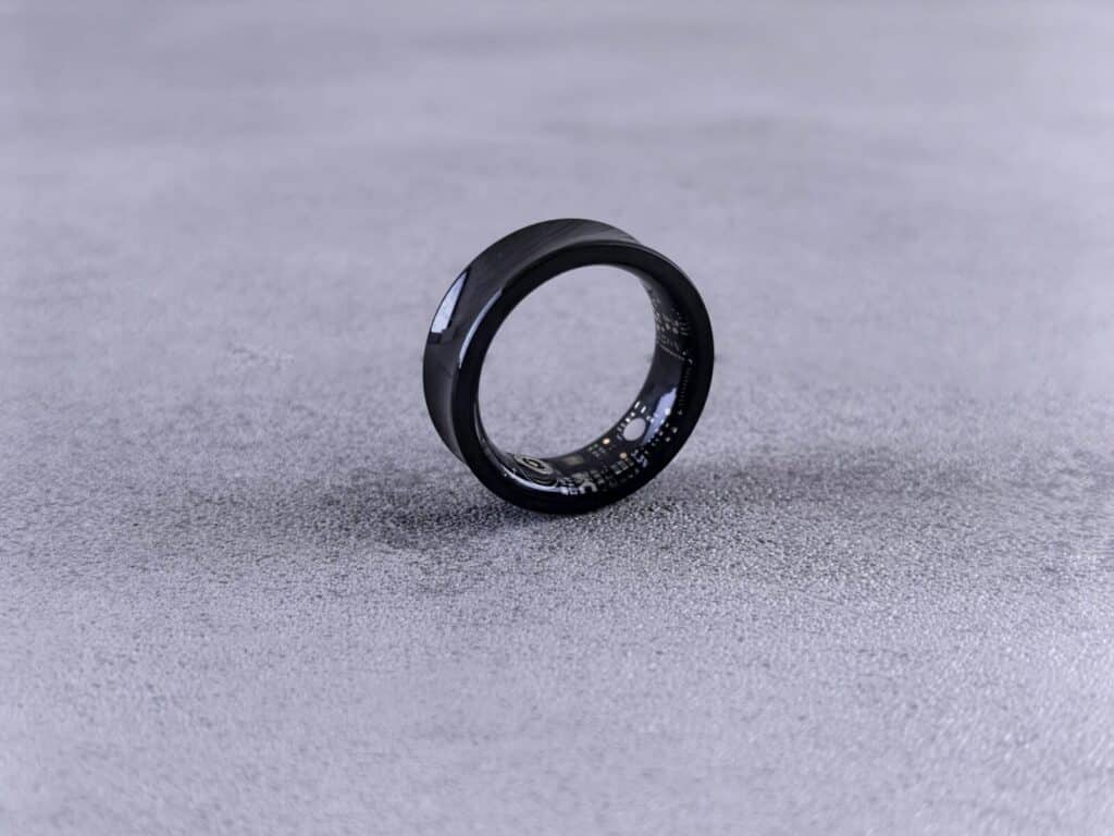 A modern black smart ring with visible circuitry resting on a textured concrete surface.