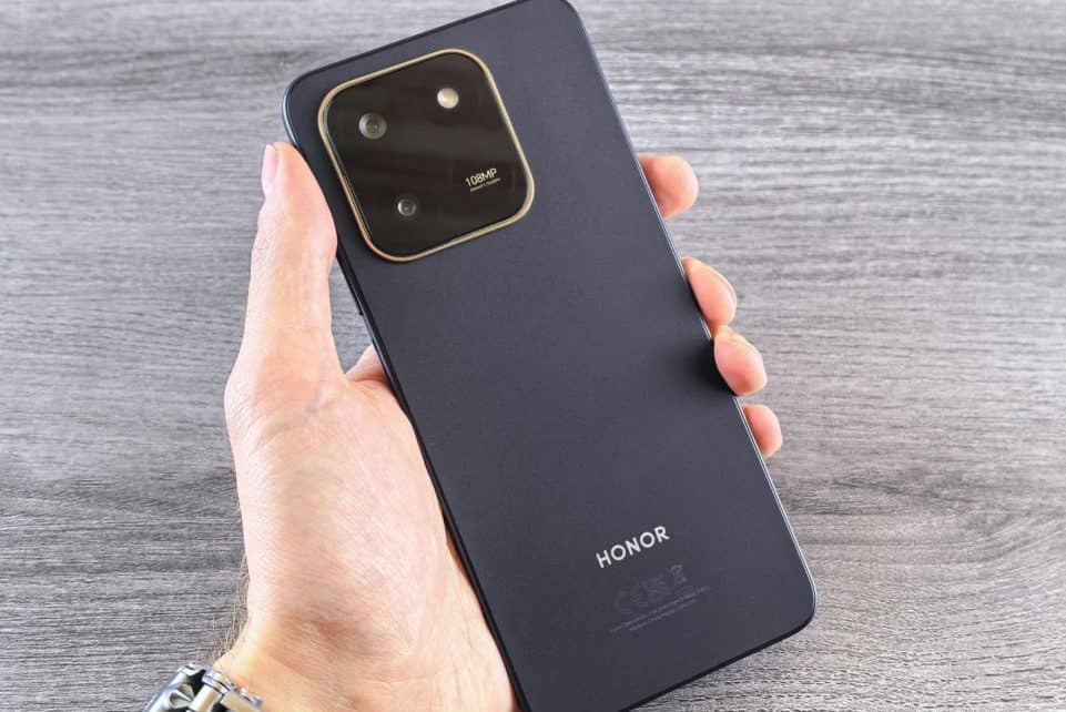 Close-up of a person holding a black smartphone with visible camera setup, shot on a wooden surface.