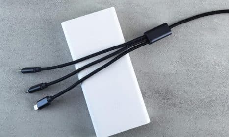 A sleek white power bank with a black multi-connector cable laid on a textured grey surface, emphasizing modern technology.