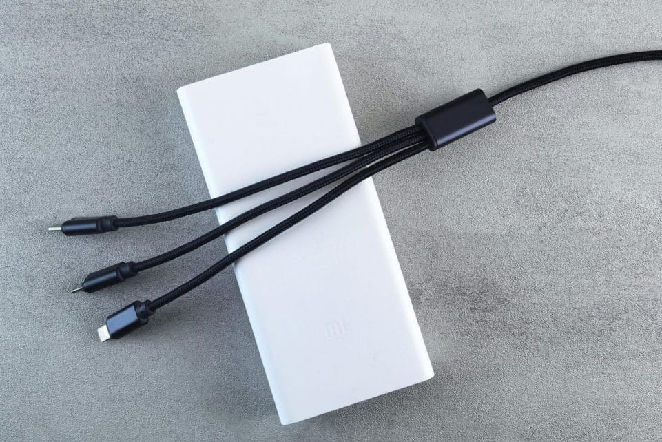 A sleek white power bank with a black multi-connector cable laid on a textured grey surface, emphasizing modern technology.