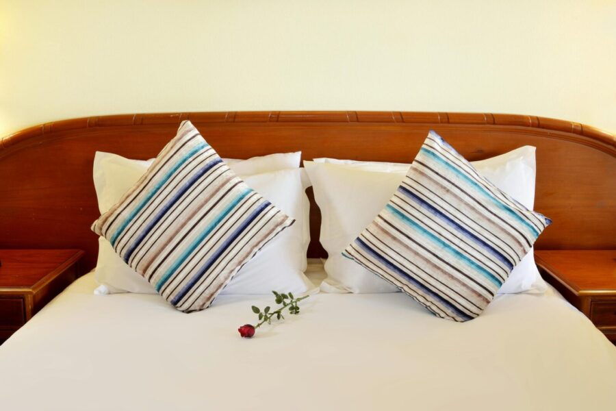 Elegant hotel bed setting with striped pillows and a red rose for a touch of romance.
