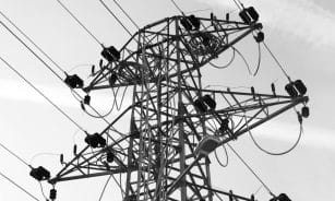 A black and white photo featuring a power line tower with cables against a clear sky.