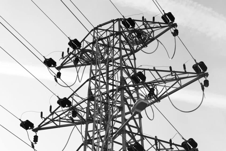 A black and white photo featuring a power line tower with cables against a clear sky.