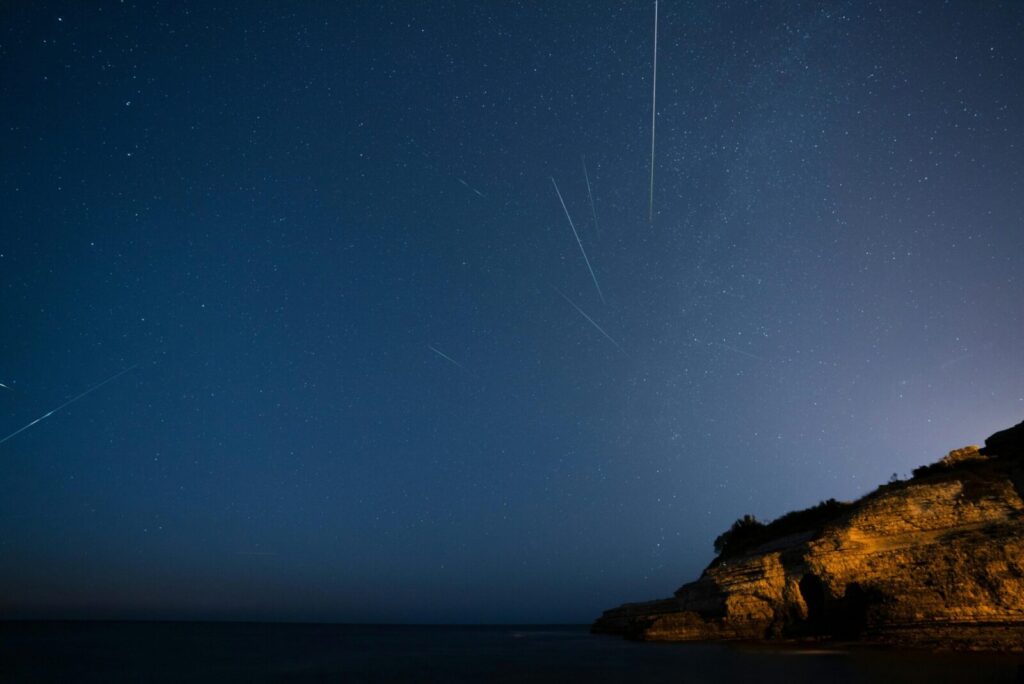 Beautiful starry sky with meteors streaking over a rocky cliff at night.