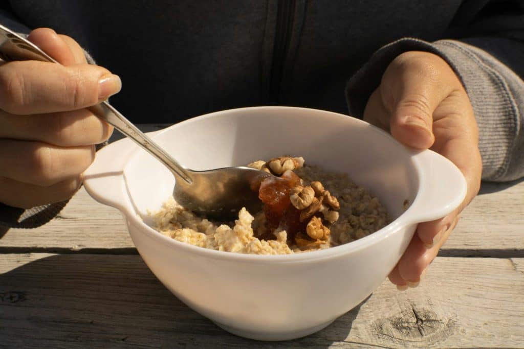 A bowl of oatmeal topped with walnuts and honey held by a person. Perfect nutritious breakfast option.