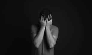 A grayscale portrait of a man covering his face, depicting emotion and mental health themes.