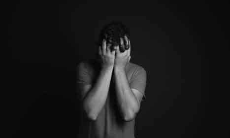 A grayscale portrait of a man covering his face, depicting emotion and mental health themes.