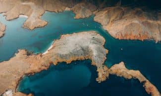 Stunning aerial view of a rugged coastal landscape in Oman showcasing turquoise waters and arid terrain.