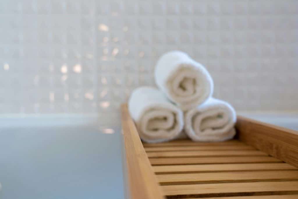 A close-up of rolled white towels on a wooden bath tray in a modern bathroom.