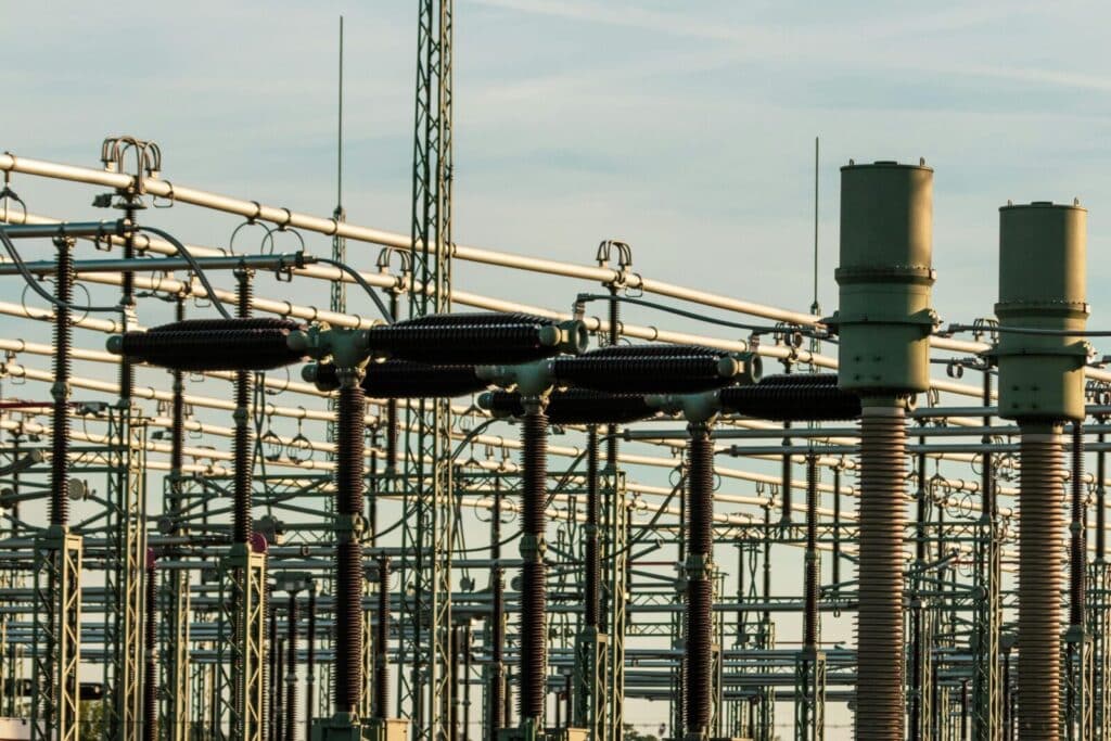 Detailed view of electrical substation with high voltage equipment and insulators against a clear sky.