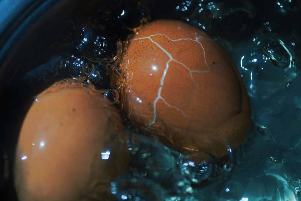 Close-up view of a cracked brown egg boiling in water, showcasing texture and cooking process.