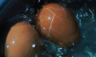 Close-up view of a cracked brown egg boiling in water, showcasing texture and cooking process.
