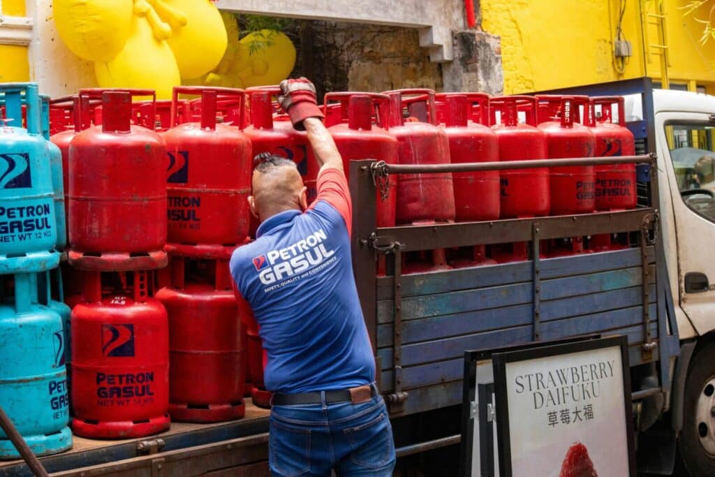 Man in uniform loading red and blue propane tanks onto a truck in urban setting.