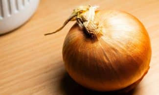 Close-up of a fresh brown onion on a wooden surface with warm lighting for culinary themes.