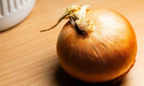 Close-up of a fresh brown onion on a wooden surface with warm lighting for culinary themes.