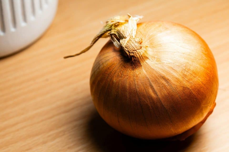 Close-up of a fresh brown onion on a wooden surface with warm lighting for culinary themes.