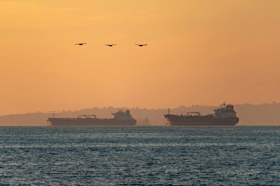 Silhouetted oil tankers on the Pacific Ocean at sunset near Long Beach, California.