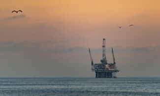Oil platform silhouetted against a vibrant sunset in Huntington Beach, California.