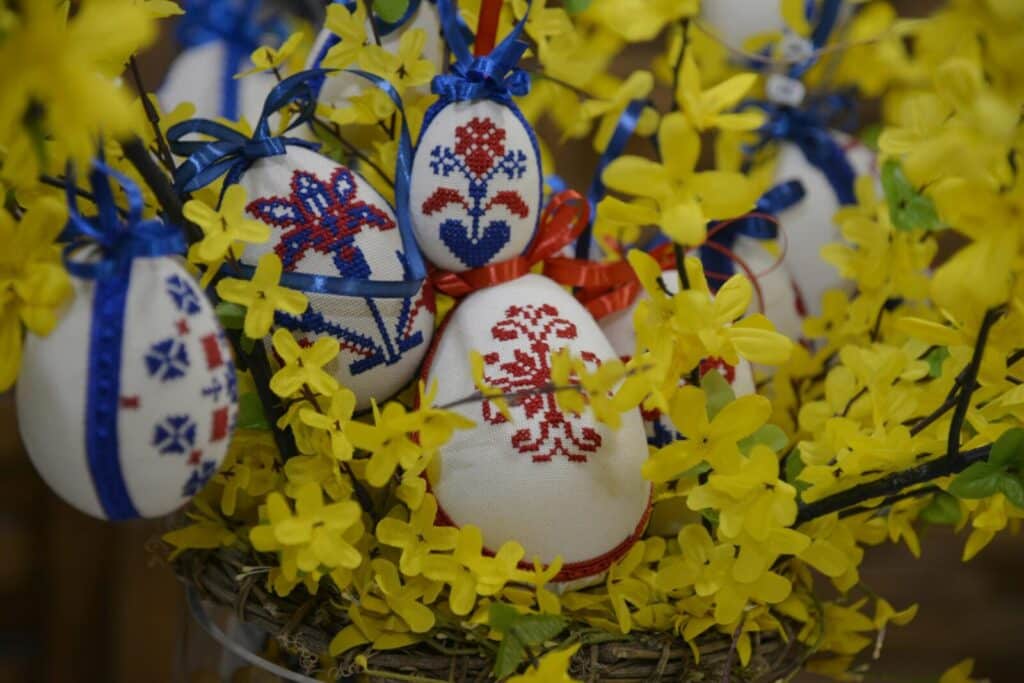 Cross-stitched Easter eggs adorned with vibrant embroidery hanging on yellow branches.
