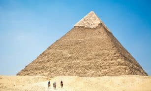 Iconic Giza Pyramid with riders on camels under bright daylight, capturing Egyptian desert landscapes.