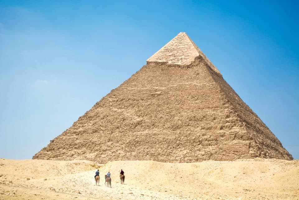 Iconic Giza Pyramid with riders on camels under bright daylight, capturing Egyptian desert landscapes.