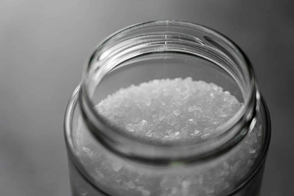 Close-up image of rock salt crystals inside an open glass jar, showcasing texture and clarity.