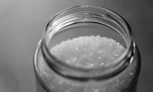 Close-up image of rock salt crystals inside an open glass jar, showcasing texture and clarity.