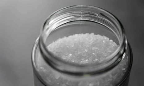 Close-up image of rock salt crystals inside an open glass jar, showcasing texture and clarity.