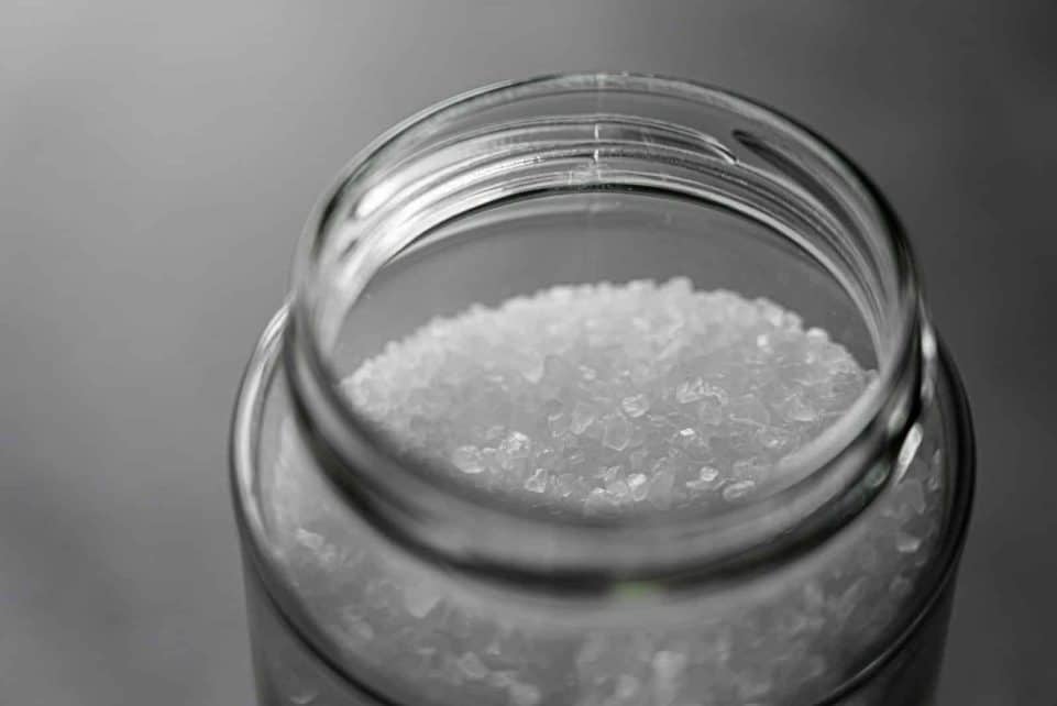 Close-up image of rock salt crystals inside an open glass jar, showcasing texture and clarity.