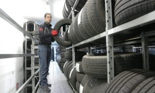 Mechanic places a tire on a rack in an indoor warehouse storage facility.