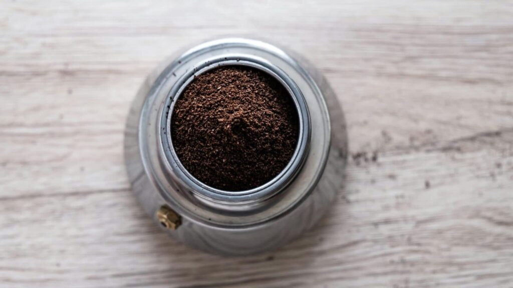 Top view of freshly ground coffee in a stainless steel container on a wooden surface.