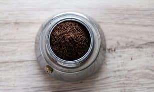 Top view of freshly ground coffee in a stainless steel container on a wooden surface.