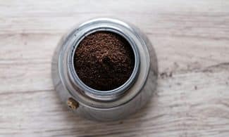 Top view of freshly ground coffee in a stainless steel container on a wooden surface.