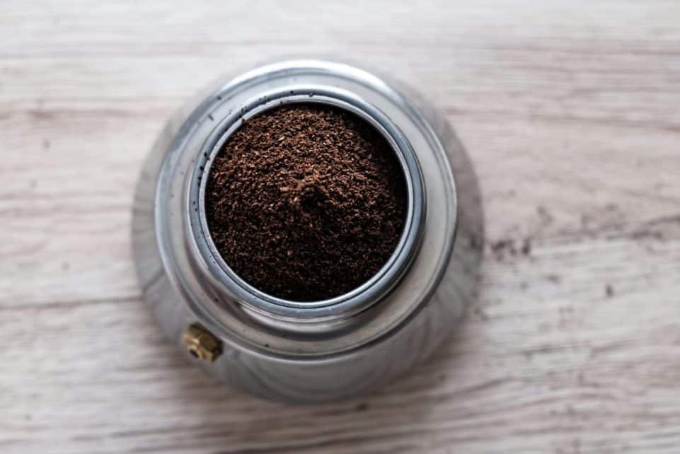Top view of freshly ground coffee in a stainless steel container on a wooden surface.
