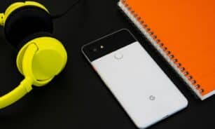 A vibrant flat lay image of a smartphone, yellow headphones, and an orange spiral notebook on a desk.