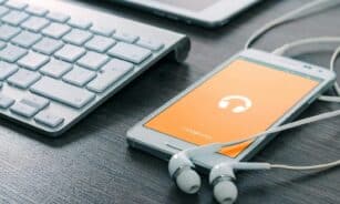 A smartphone with earphones connected alongside a keyboard on a wooden desk, showcasing modern technology.