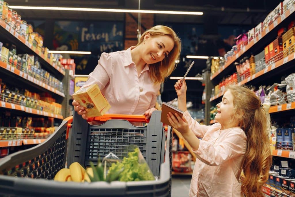 Mother and daughter enjoying shopping at the supermarket with a checklist and cart.