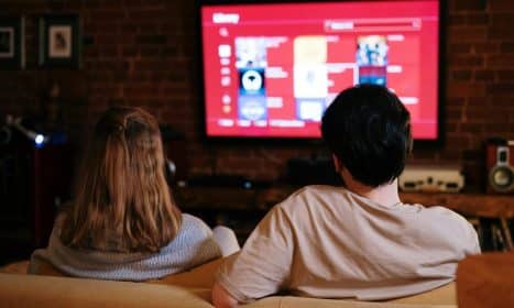 A couple enjoys streaming shows on a large TV in a cozy, brick-walled living room.