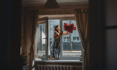 A woman cleaning a window in a well-designed cozy apartment with curtains and natural light.