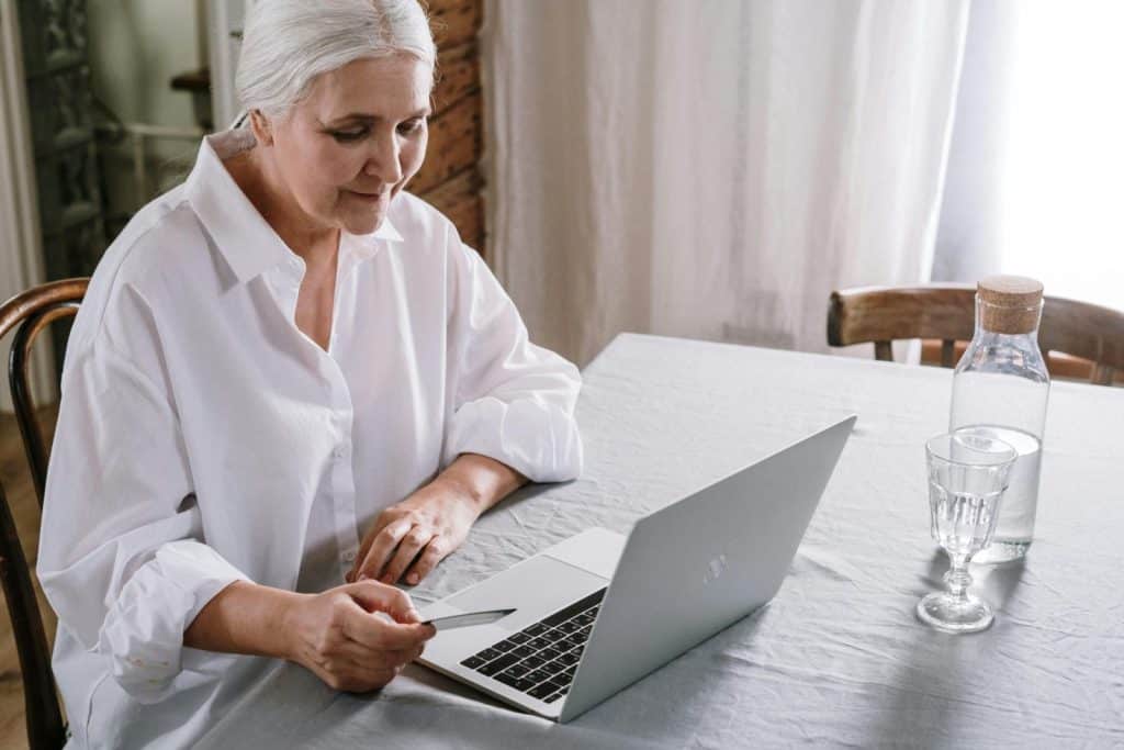 Elderly woman using laptop for online shopping at home during daytime.