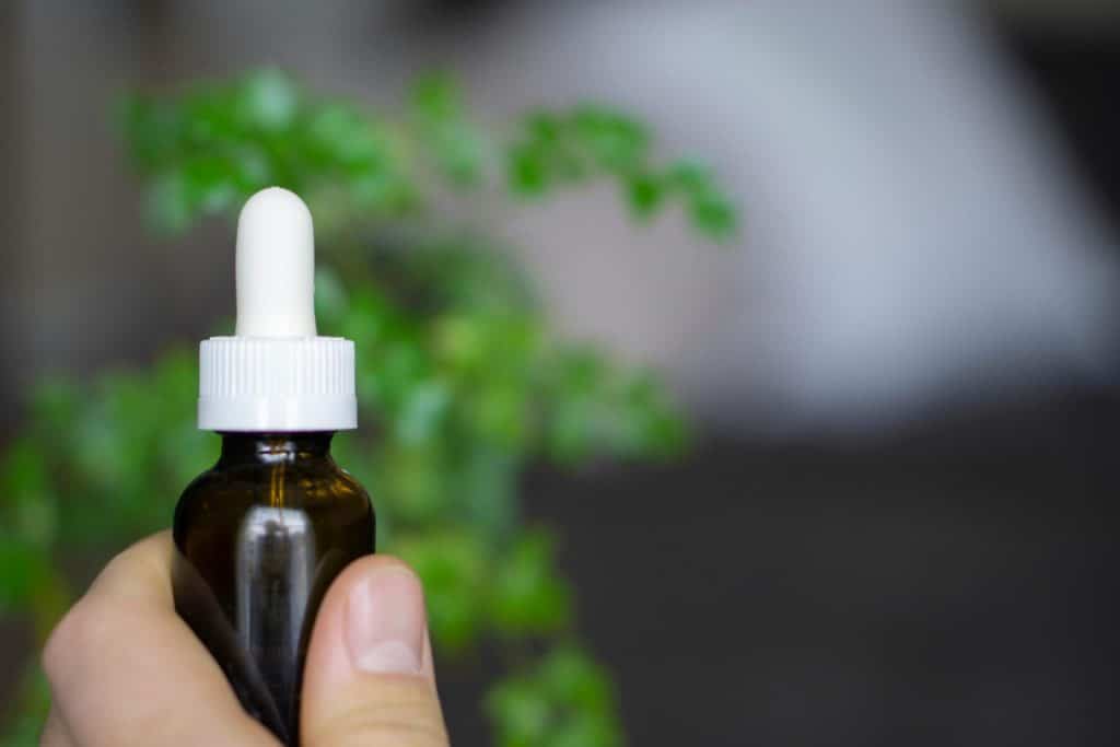 Hand holding a dropper bottle of CBD oil against a soft-focus botanical background.