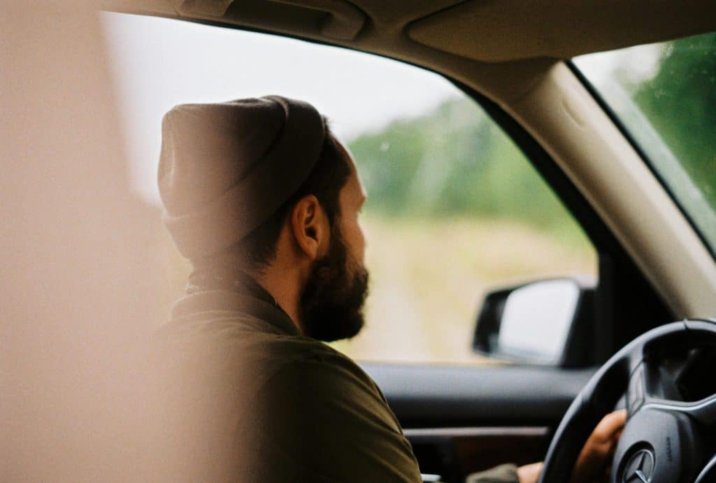 Bearded man wearing a beanie drives a car with blurred background.