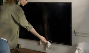 A woman cleaning a black screen TV in a cozy home environment, promoting cleanliness.