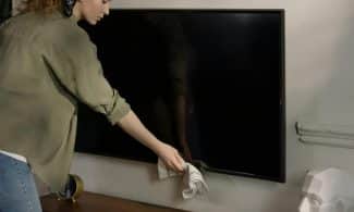 A woman cleaning a black screen TV in a cozy home environment, promoting cleanliness.